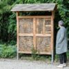 Insectenwand op een bedrijventerrrein. Een oudere dame met een grijze jas kijkt naar de insectenwand van Vivara Pro.
