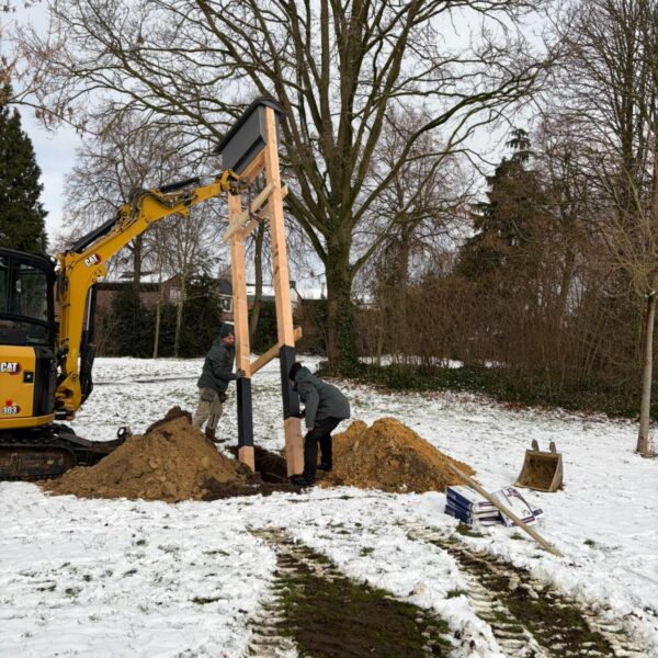 Weert_Paalkast_Vleermuis_Plaatsing In afbeelding van twee mannen en een graafmachine die een paalkast c.q. kraamkast voor vleermuizen plaatsen in de sneeuw ergens in een park in de gemeente Weert.